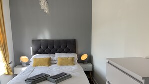 Ein ordentlich bezogenes Bett mit weißer Bettwäsche, zwei Nachttischlampen und einem grauen Kopfteil.