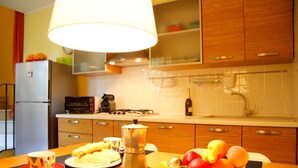 Una cocina moderna con refrigerador, estufa y microondas. Hay una mesa con una cafetera y una botella de vino.