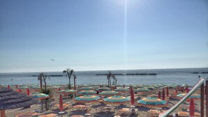 Una playa con hileras de sombrillas y tumbonas, cielo despejado y mar tranquilo.