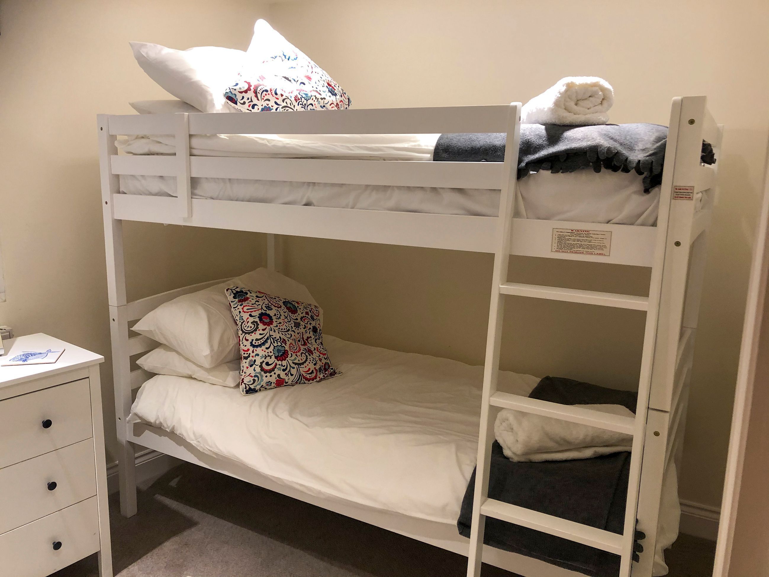 Un lit superposé avec une literie blanche et des coussins décoratifs.