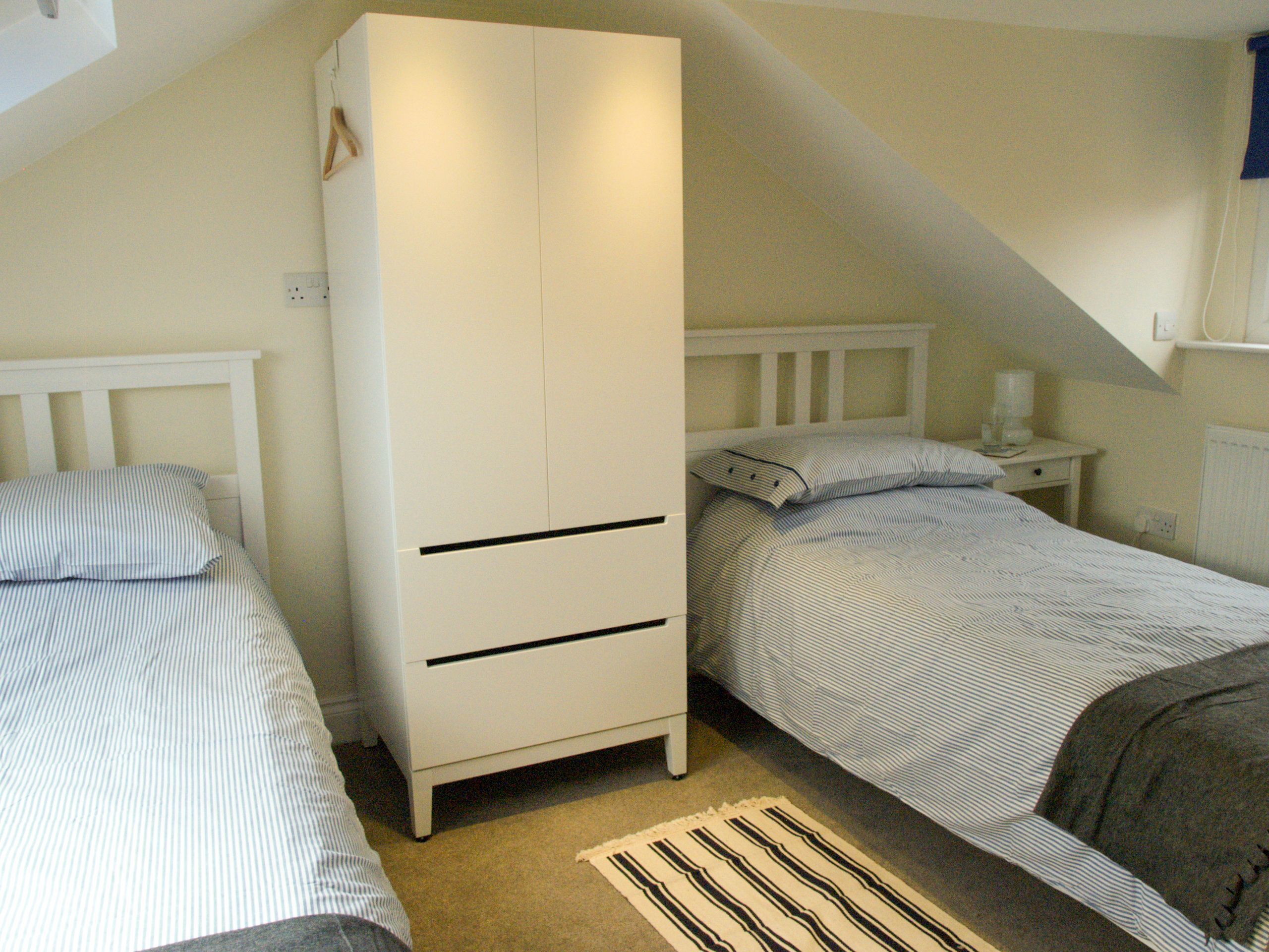 A bedroom with two single beds, a white wardrobe, a nightstand, and a radiator.