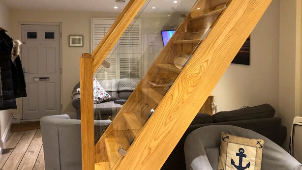 A wooden staircase with glass railings, a grey sofa with an anchor pillow, and a television in the background. - 3 bedroom accommodation in Cowes (Cowes)