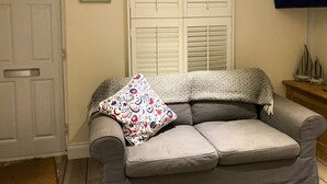 A living room with a grey sofa, a patterned throw pillow, a white door, and a television on a wooden stand. - 3 bedroom accommodation in Cowes (Cowes)