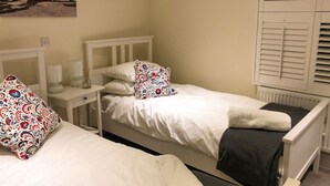 A bedroom with two single beds, white headboards, and a nightstand with lamps. - 3 bedroom accommodation in Cowes (Cowes)