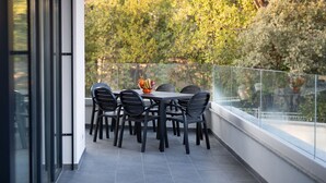 A balcony with a table and chairs, a fruit bowl, and a view of trees.