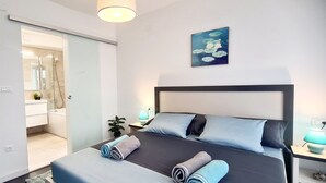 A modern hotel room with a bed, bedside tables, a nightstand, a lamp, and a painting on the wall.