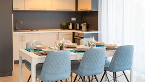 A modern kitchen with white cabinets, a dining table set with blue chairs, and a pendant light above.