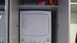A compact, built-in washer and dryer unit with a control panel and a shelf above containing cleaning products.