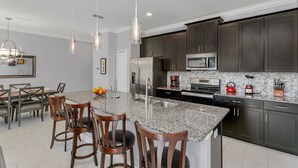 Une cuisine moderne dotée de plans de travail en granit, de meubles de couleur sombre, d’appareils électroménagers en acier inoxydable et de luminaires suspendus.