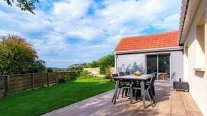 Un patio con una mesa y sillas, una terraza de madera y una casa con techo rojo.
