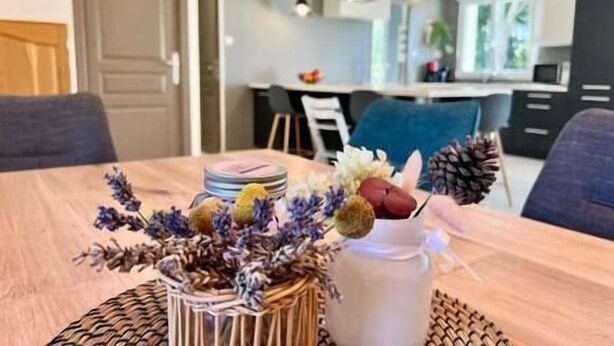 Una mesa de comedor con un centro de flores secas y piñas, un jarrón blanco y un mantel tejido.