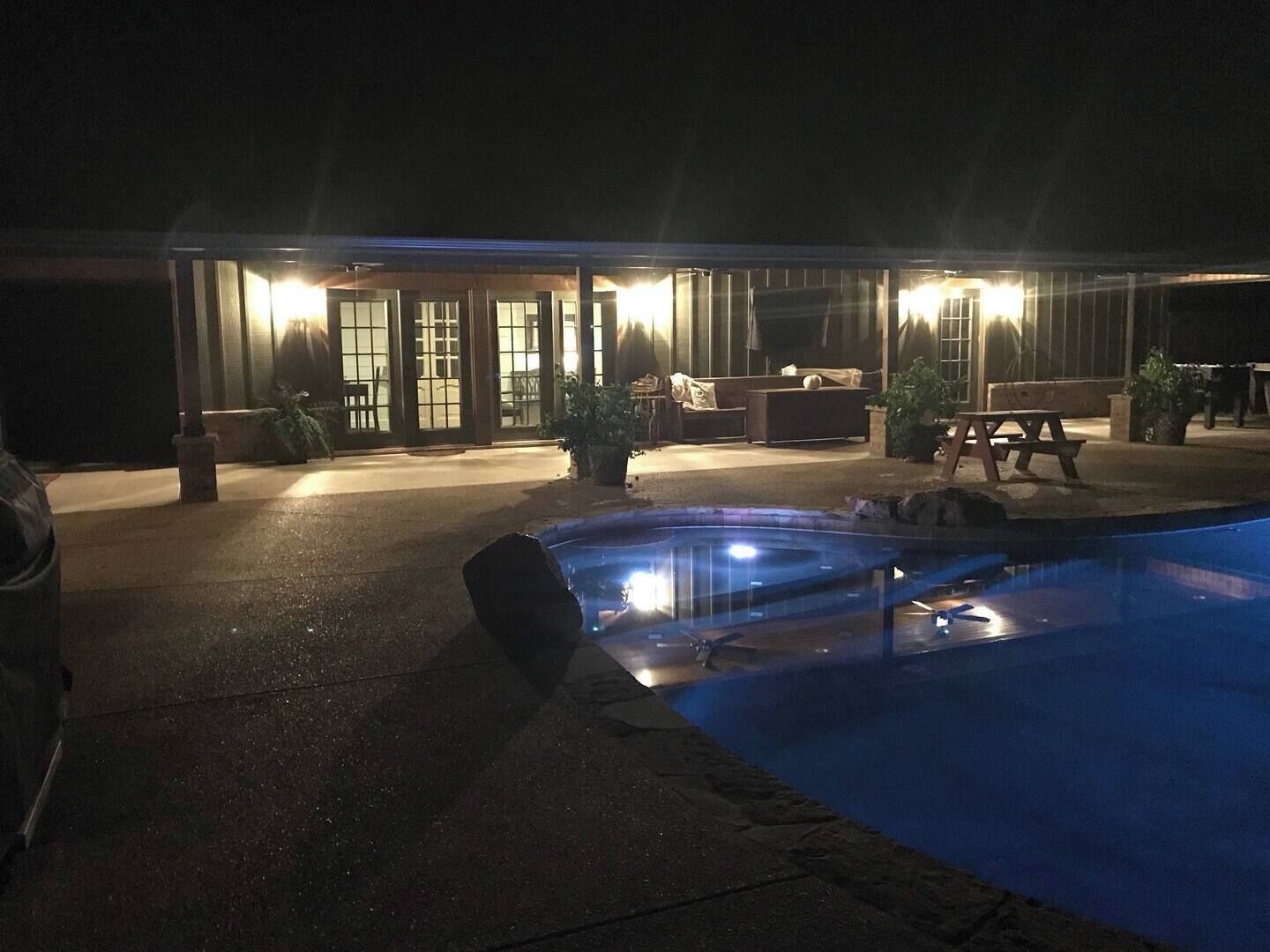 Zona de piscina con jacuzzi, mobiliario exterior y un edificio con amplios ventanales y puertas.