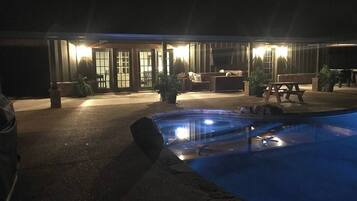 Zona de piscina con jacuzzi, mobiliario exterior y un edificio con amplios ventanales y puertas.