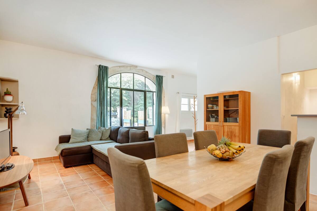 Een moderne woonkamer met een eethoek, een bank, een tafel met stoelen en een groot raam met gordijnen.
