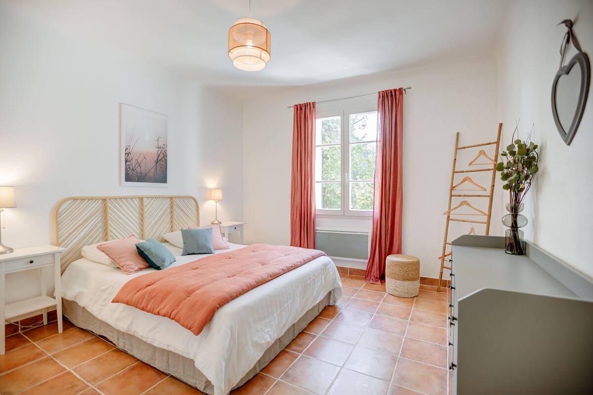Een slaapkamer met een bed, nachtkastjes, een raam met gordijnen, een hangplant en een wandladder.