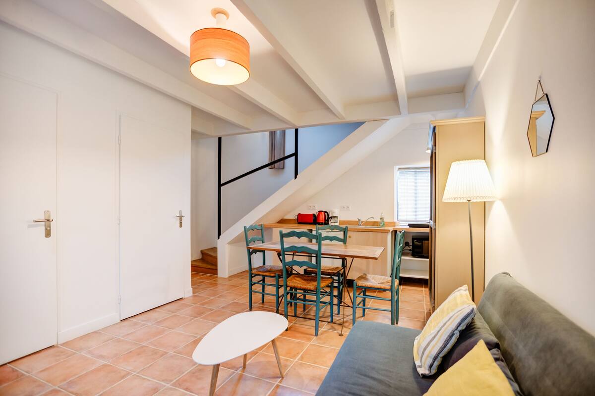 Een gezellige woonruimte met een bank, een kleine tafel en een eettafel met stoelen. Een trap leidt naar een hoger niveau.