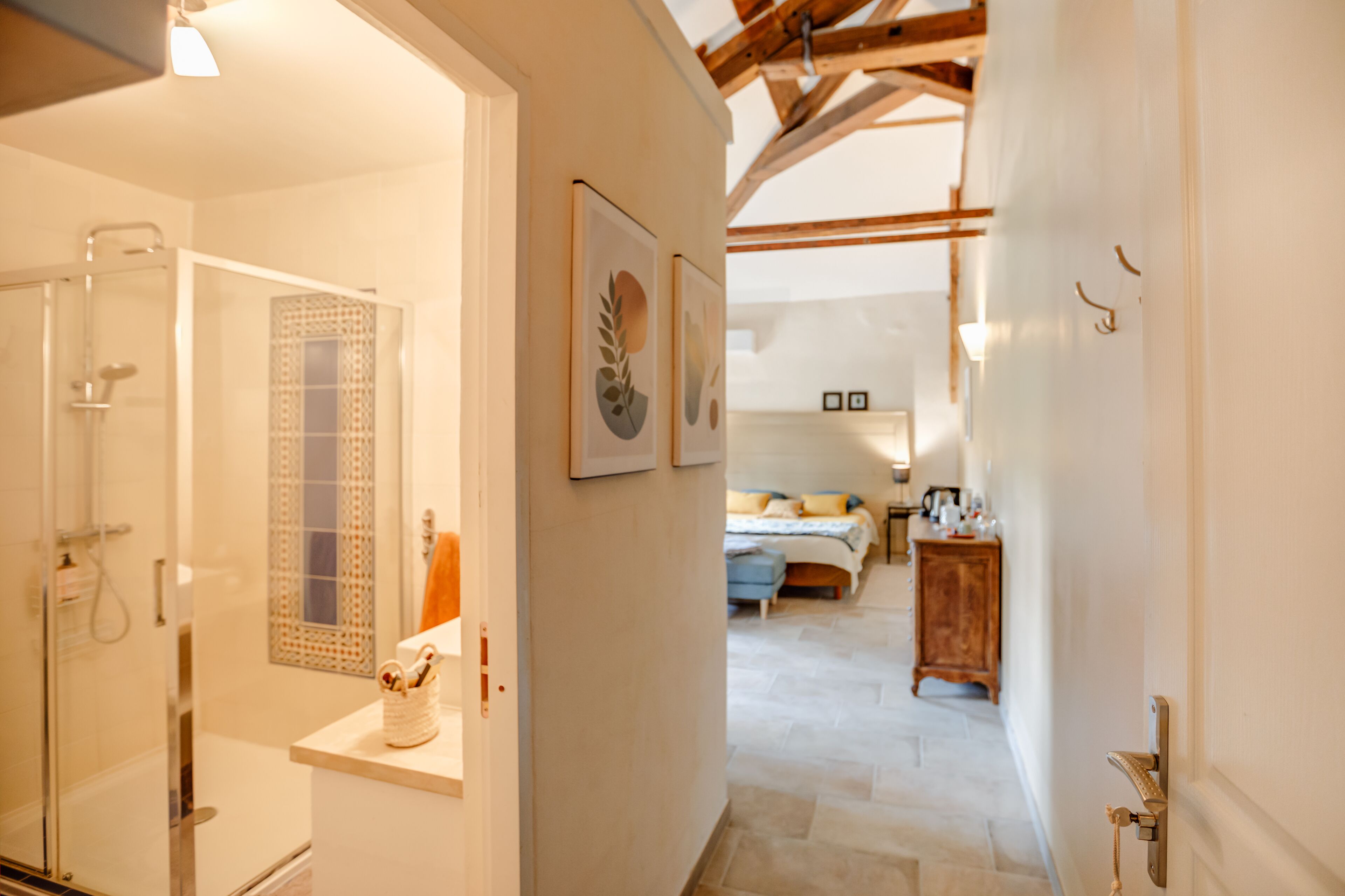 A hallway leading to a bedroom with a bed, a wooden cabinet, and a bathroom with a shower.