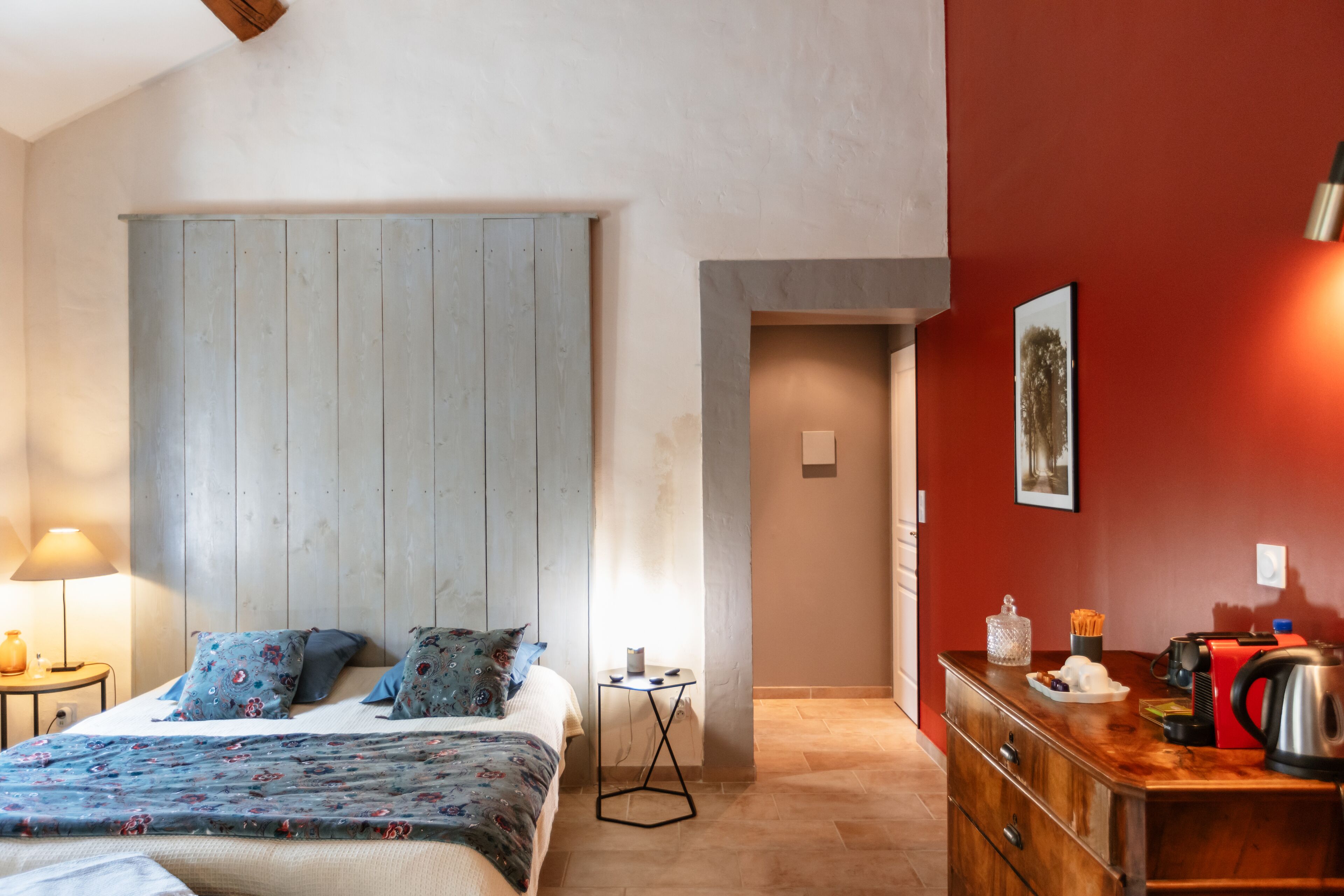 A bedroom with a bed, a bedside table, a dresser, and a red wall.
