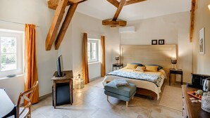 Une chambre avec un plafond en bois, un lit avec une tête de lit, un bureau avec un ordinateur et une fenêtre avec des rideaux.
