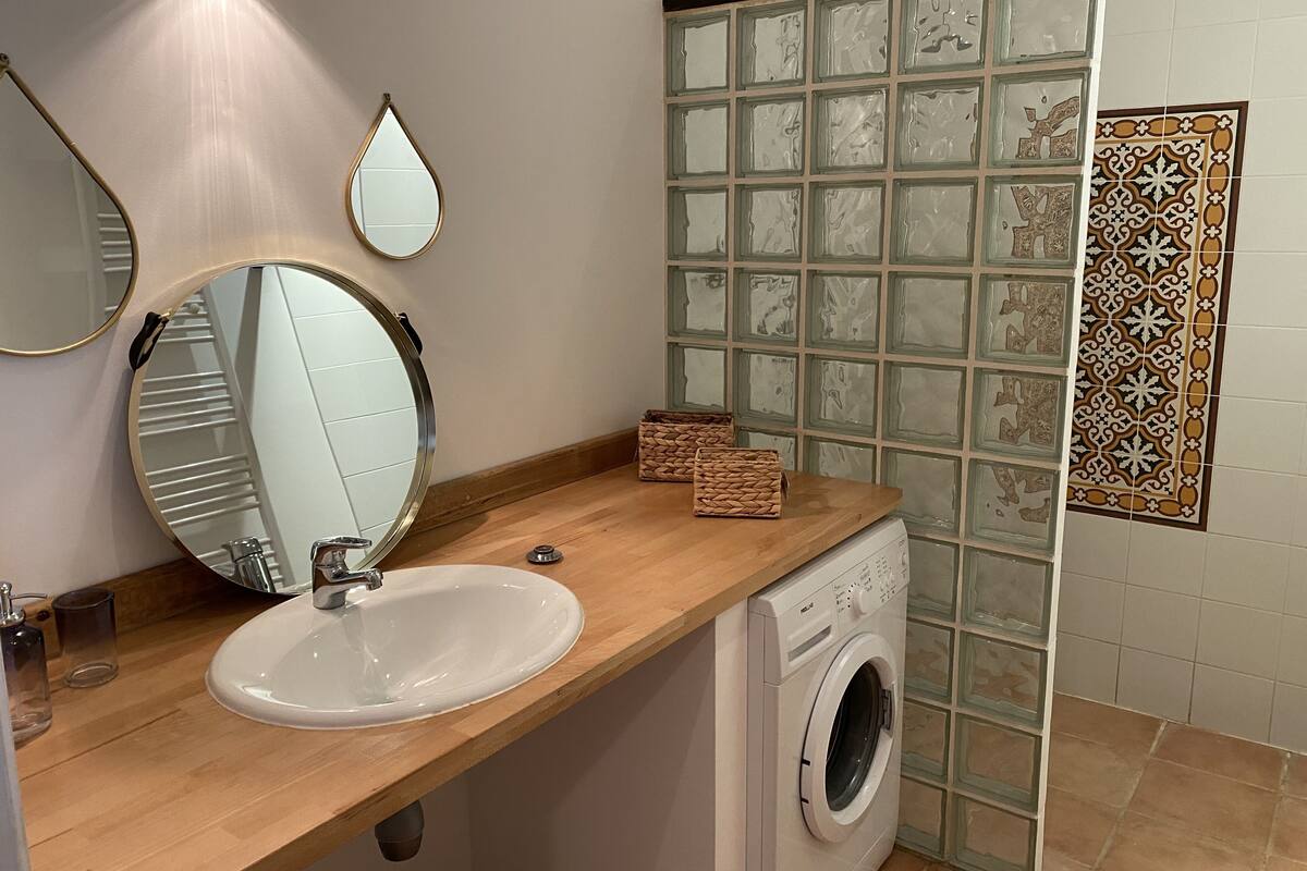 Een badkamer met een houten wastafelmeubel, een wastafel, een spiegel, een wasmachine en decoratieve tegels.