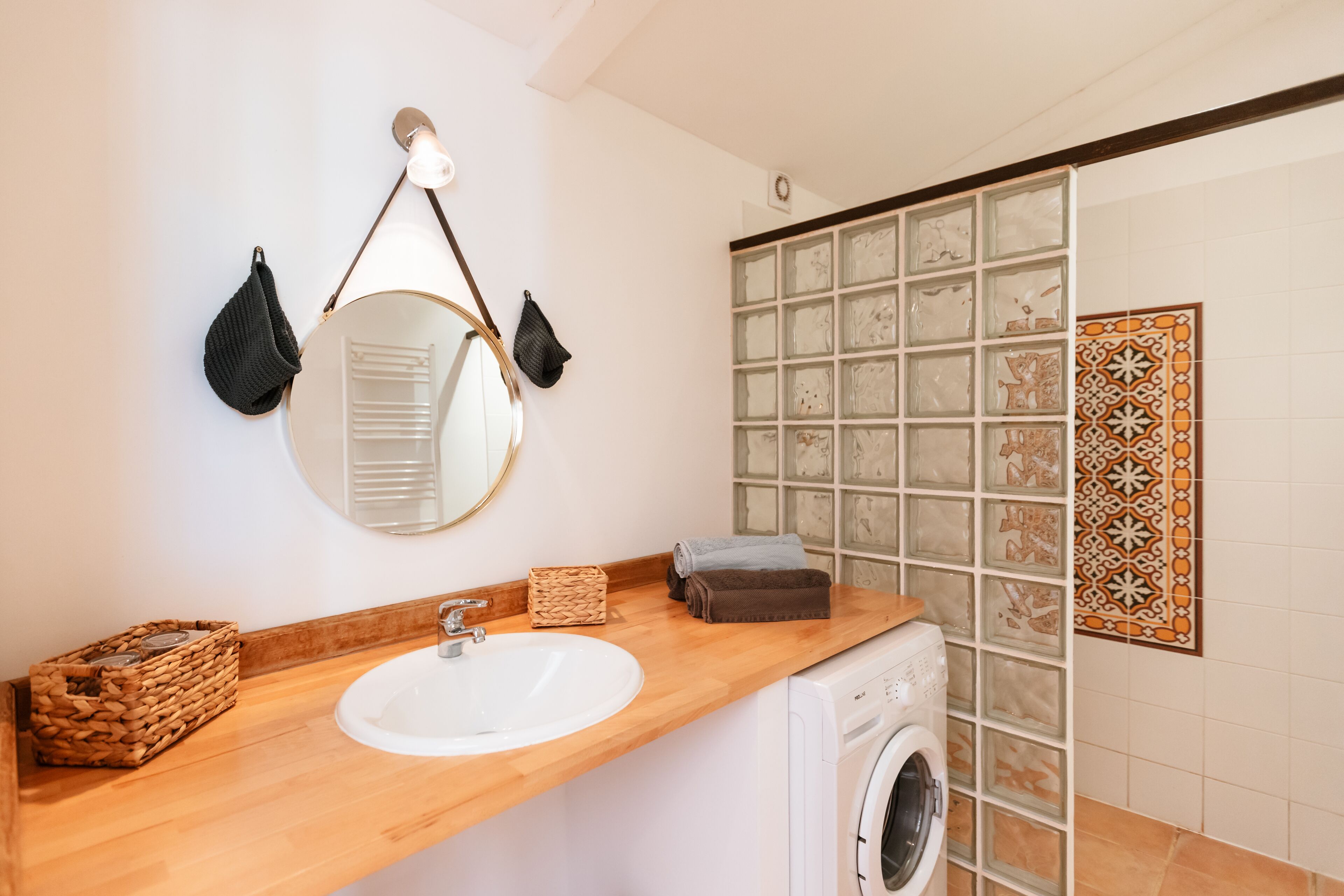 A bathroom with a wooden countertop, a sink, a washing machine, and a mirror with towels hanging on it.