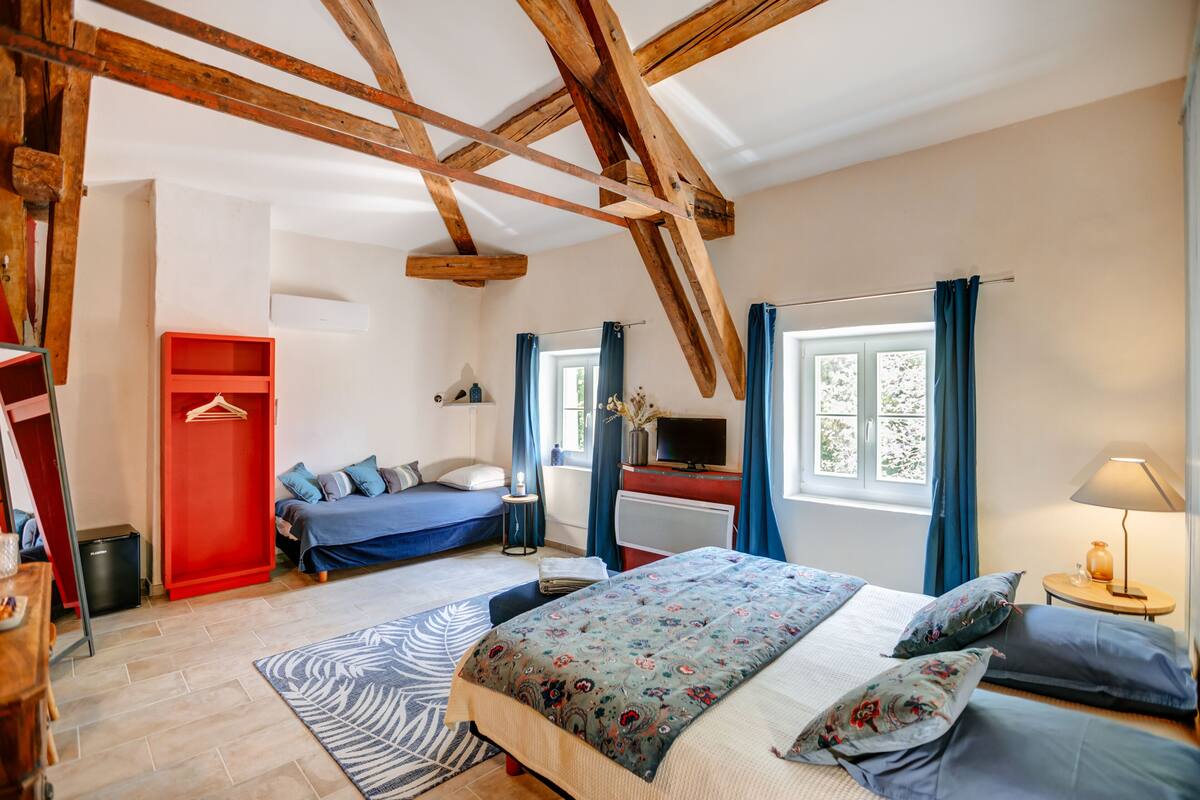 Een slaapkamer met een bed, een bureau, een stoel, een rode garderobe en een raam met gordijnen.