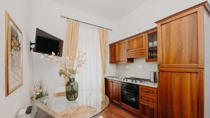 Une cuisine compacte avec des meubles en bois, une cuisinière à gaz et une table à manger en verre, accompagnée de chaises.