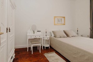 Un dormitorio con cama, mesita de noche, cómoda, espejo y un cuadro en la pared.