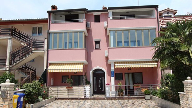 Un bâtiment rose à deux étages, doté d’une entrée carrelée, d’un escalier et d’un balcon.
