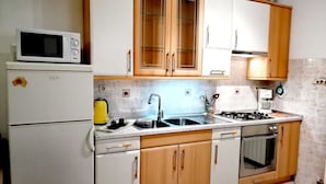Une cuisine de taille réduite, dotée d’appareils électroménagers blancs, de meubles en bois et d’un dosseret carrelé.