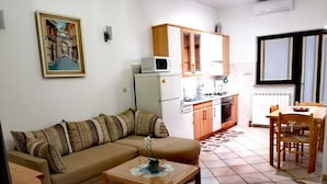 Un espace de vie compact comprenant un canapé, une petite table, un coin cuisine avec des placards et des appareils électroménagers, ainsi qu’une table à manger avec des chaises.