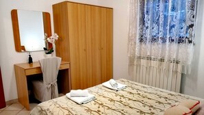 Une chambre à coucher comprenant un lit, une armoire en bois, un bureau avec une chaise, un miroir et une fenêtre ornée de rideaux en dentelle.