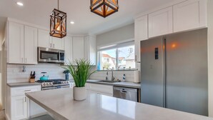 A modern kitchen with white cabinets, stainless steel appliances, a large island, and a view of the outside.