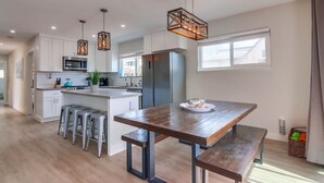 A modern kitchen with stainless steel appliances, a wooden island with bar stools, pendant lighting, and a large window providing natural light.
