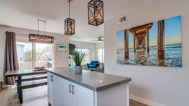 A modern kitchen with a central island, pendant lighting, and a large ocean-themed painting on the wall.