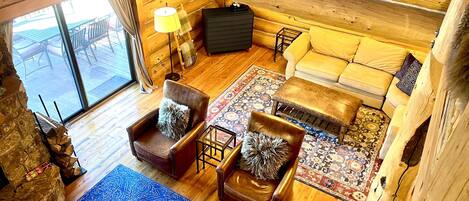 L'interno accogliente di una baita con travi a vista in legno, un divano, due poltrone, un tappeto decorato e un'ampia finestra.