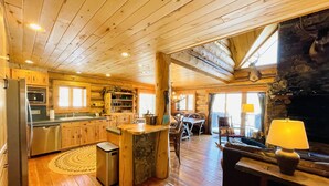 Interior espaçoso de cabana com soalho de madeira, cozinha, área de refeições e lareira.