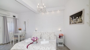 Een moderne slaapkamer met een groot bed, een kroonluchter, een eethoek met een tafel en stoelen, en een schilderij aan de muur.