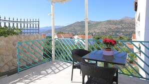 A balcony with a table and chairs, a potted plant, and a view of a mountainous landscape.
