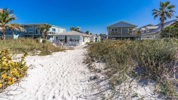 A beachfront property with a sandy path leading to houses, surrounded by vegetation.