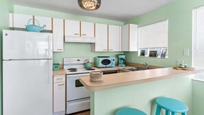 A kitchen with a refrigerator, stove, microwave, and a small island with stools.