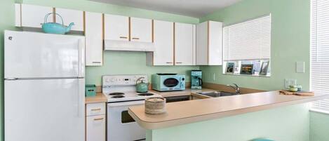 A kitchen with a refrigerator, stove, microwave, and a small island with stools.