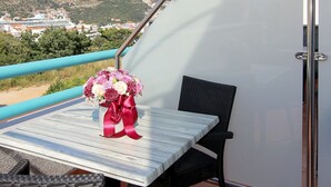 Un balcon avec une table et des chaises, un bouquet de fleurs et une vue sur un navire de croisière et le paysage environnant.