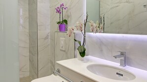 Une salle de bain moderne avec un lavabo blanc, des murs en marbre et des toilettes.