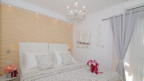 Quarto com cama, lustre, mesa de cabeceira com flores e janela com cortinas.