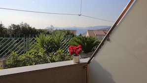 Varanda com vista para montanhas distantes, grade de metal e vegetação.