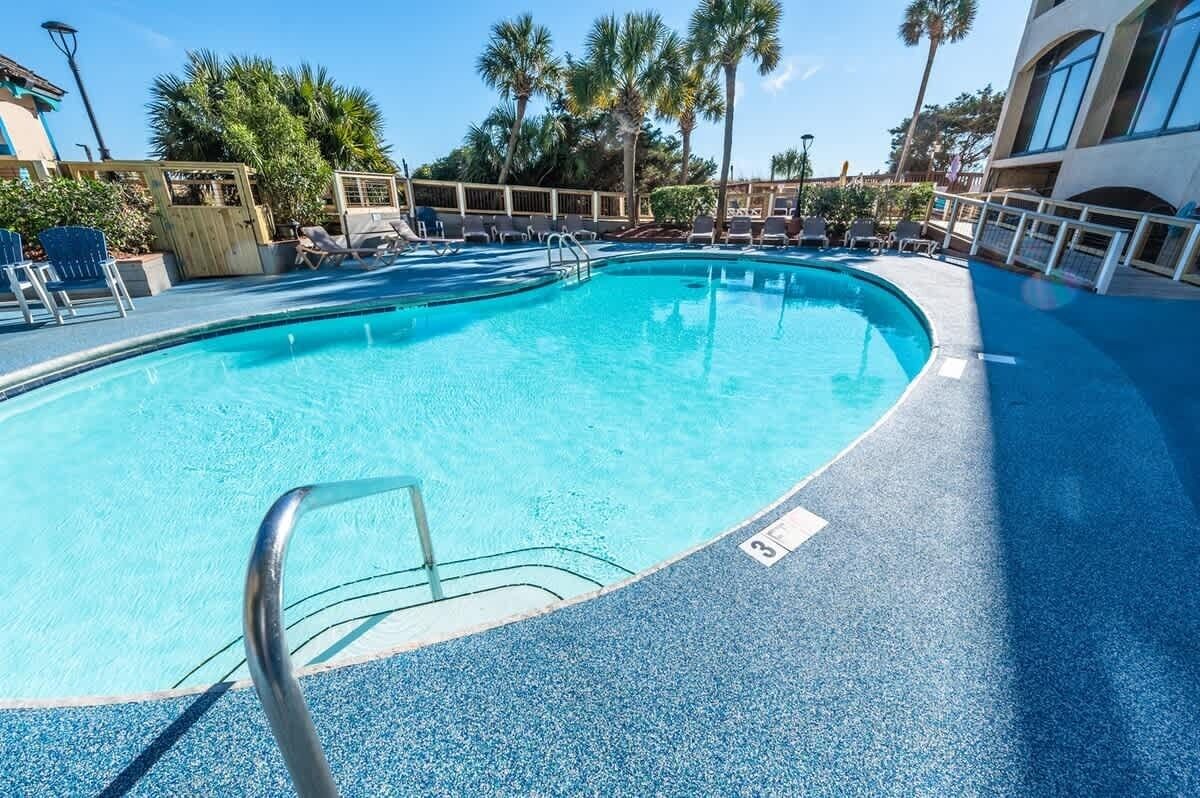 A pool area with lounge chairs and a clear blue pool.