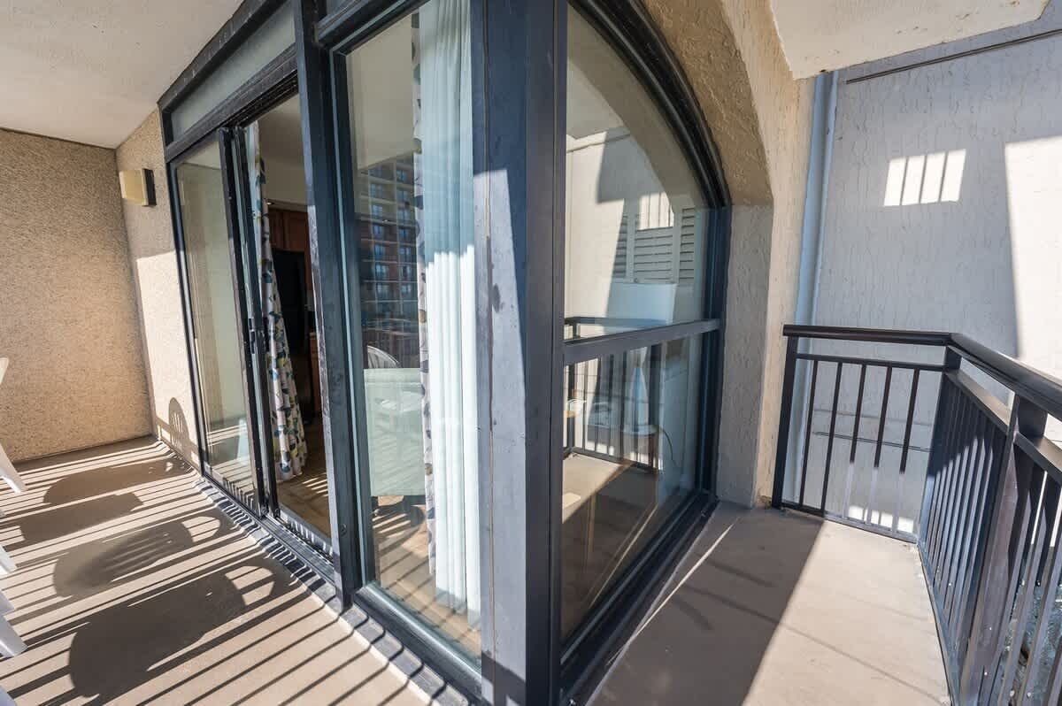 A balcony with a glass door leading to a room.