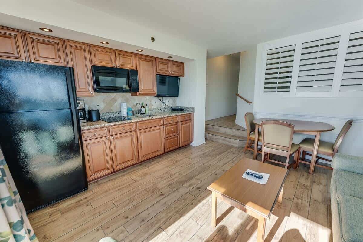 A compact kitchen with wooden cabinets, a black refrigerator, a microwave, and a small dining area with a table and chairs.