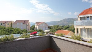 A residential area with houses, a balcony with plants, and a mountainous backdrop.